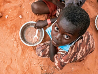 A child eating gruel on the ground, representing how many children still go hungry and lack access to basic necessities