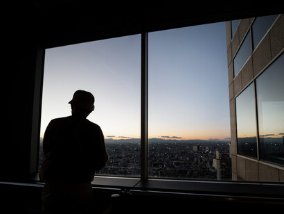 Face à la ville qui s’étend sans fin, une silhouette contemple le monde devenu silencieux. Là où autrefois s’ouvraient les portes avec un sourire, ne restent plus que des fenêtres à distance