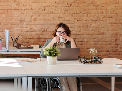 A woman in a wheelchair smiling while engaging with her laptop, reflecting empowerment and the seamless integration of technology into her daily life
