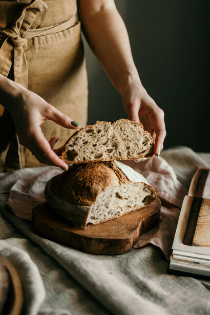 A woman stands at a table with a freshly baked loaf of homemade sourdough bread