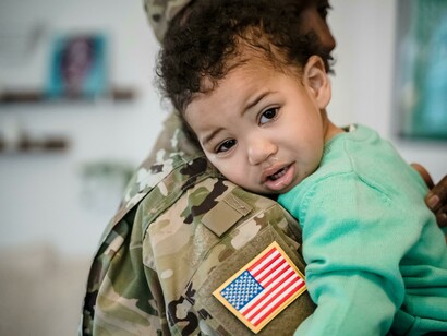A soldier walks away with his family, carrying his child in his arms