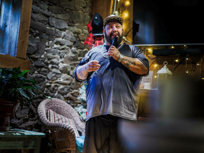 An open-mic stand-up act features a Latino comedian performing at a private country club