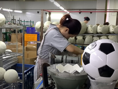 A woman is working diligently on producing footballs