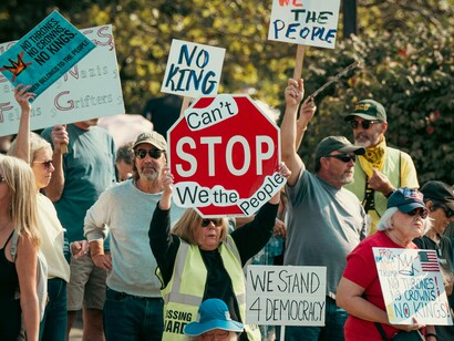 A woman elevating a “We the People” placard above her head, representing sovereignty anchored in the public