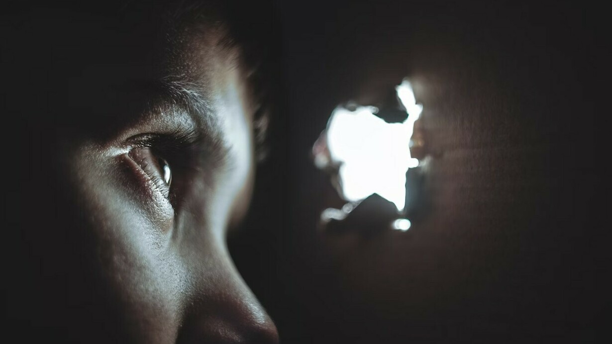 A person peering through a hole with a look of fear and uncertainty
