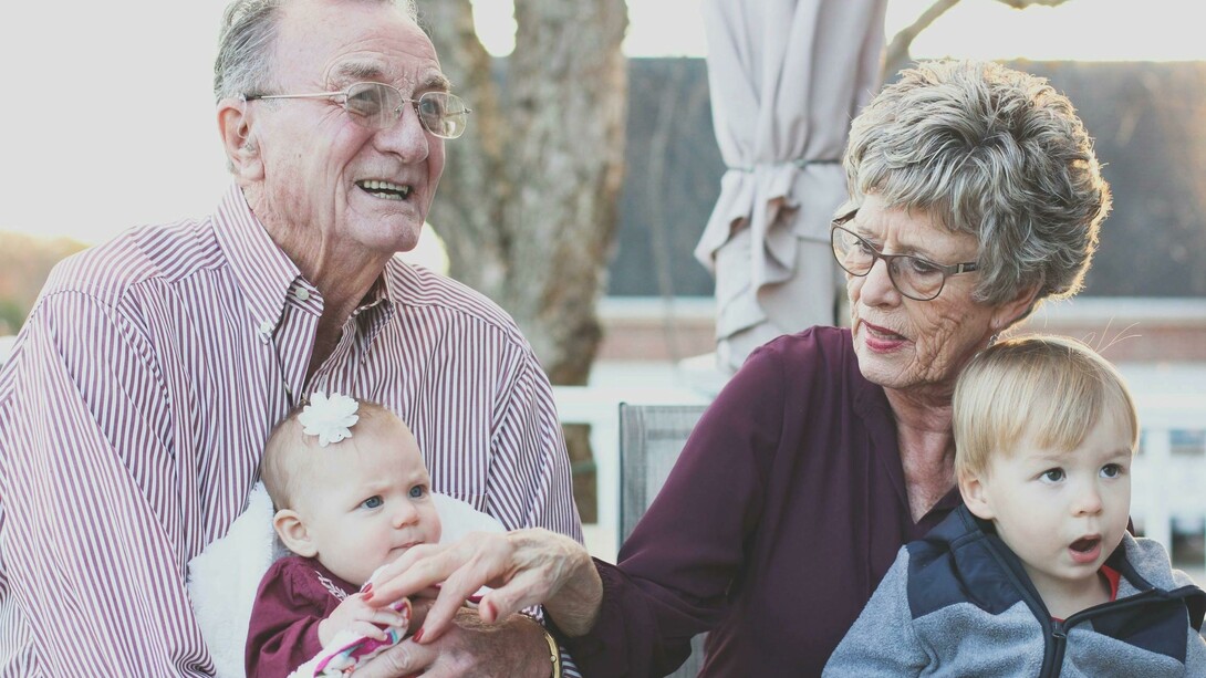An elderly grandmother and grandfather lovingly hold their grandchild on their lap