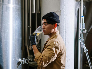 Dressed in a brown jacket and knit cap, the man enjoys a fresh pour of craft beer