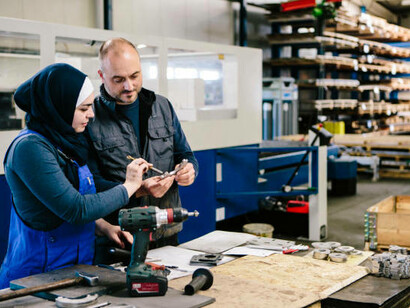 A young female technician collaborates with a male colleague in a workshop, using work tools, Germany