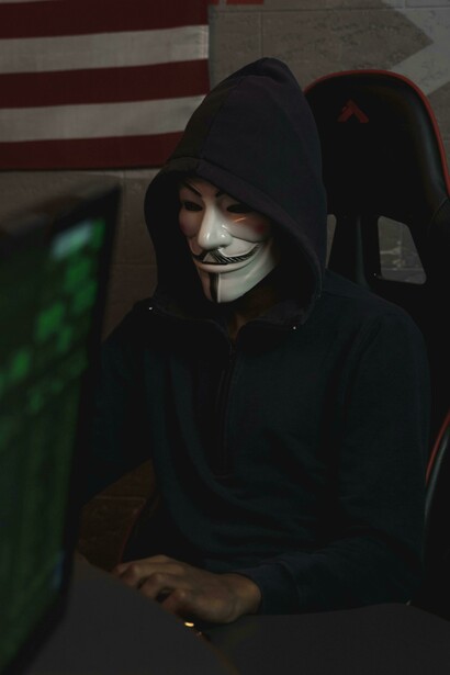 A hooded figure at a computer represents disinformation and sabotage in cyberspace