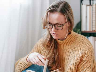 At home in her sweater and glasses, a woman dives into a good book, surrounded by warmth and the quiet joy of reading