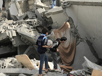 Children standing beside a collapsed building in Gaza, amidst the destruction caused by residential bombings and the ongoing humanitarian crisis