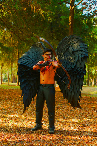 A shirtless man dressed as an angel, bow in hand, his symbolic wings evoking a fallen-angel aesthetic
