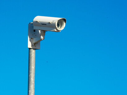 A white CCTV security cameras fixed to a black pole, standing against a clear blue sky