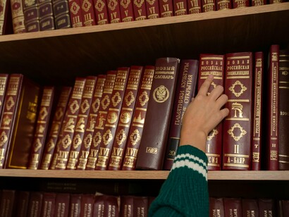 Pessoa seleciona livro de enciclopédia em uma prateleira. Louis parou por um momento: não havia pensado nisso. De fato, não adiantaria apenas "ocidentalizar" o Egito, com características estéticas e até nomes que remetessem àquele país em seu apogeu, mas teria de pensar em questões fundamentais, como os idiomas