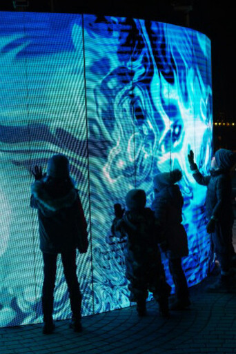 Visitors admire a vibrant blue light art display on a wall during an evening event in Oslo, Norway