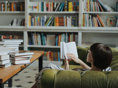 In the warm, library-like atmosphere of a cozy bookstore, a woman searches through a stack of books, lost in her love for reading