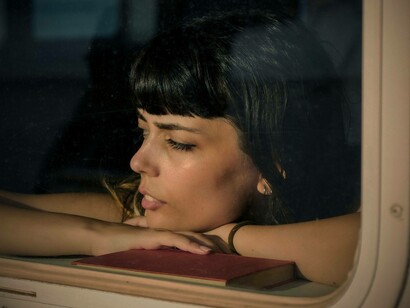 Donna che guarda al di fuori del finestrino in treno, con un libro accanto: "La coppia di fronte a Didi si era messa nel frattempo a leggere Flaubert, la donna aveva appoggiato la sua testa sulla spalla dell’uomo e di tanto in tanto chiudeva gli occhi, assorta, in ascolto"