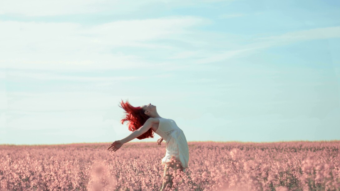 A woman in a yellow dress stands in a field covered with pink petals
