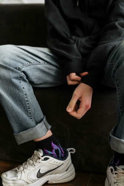 A teenage boy wearing a black jacket and gray jeans, his scarred hands resting in his lap—capturing the hidden pain and mental health challenges many teens silently endure