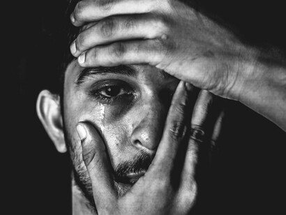 A man with tears streaming down while hands constrain his face, showing how grief often grasps us hard