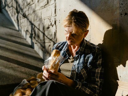 Persona senza fissa dimora che mangia un panino. L'autrice invita ad alzare lo sguardo e a riconoscere ogni persona come una presenza, non come un numero