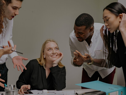 During a business meeting, a woman wearing headphones appears disengaged while the rest of the team discusses