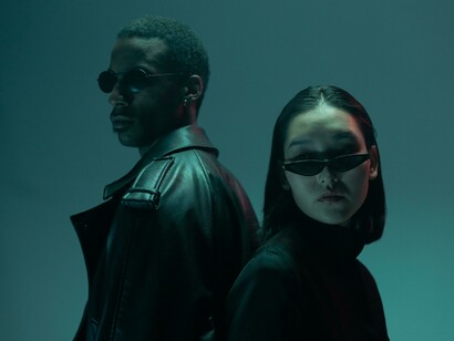 Man and woman stand back to back, holding guns in a Matrix-like universe where machines have enslaved humanity