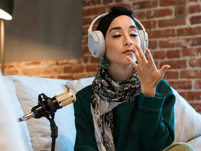 A woman with white headphones speaking into a microphone, recording her podcast as a content creator