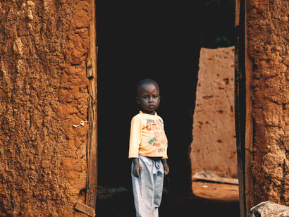 A young kid standing in the doorway of his mud house, providing a stark contrast to the modern skyscrapers that grace the cities of South Africa