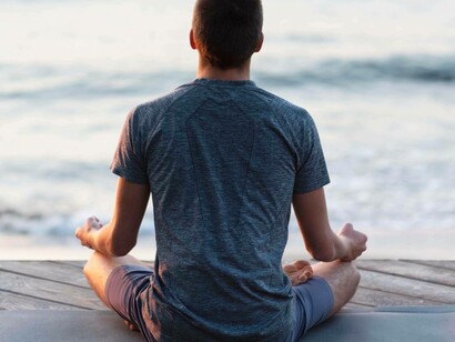 Vista posteriore di un uomo seduto che medita in posizione del loto su un pontile di legno