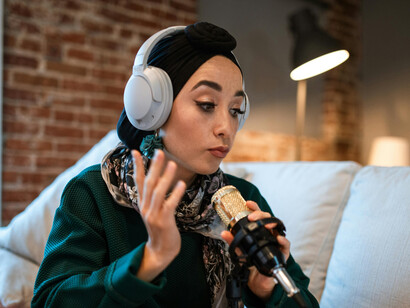A woman wearing white headphones, speaking into a microphone as she records a podcast, embodying the role of a content creator