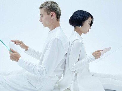 A man and a woman seated back to back with tablets in their hands, symbolizing the silent distance that digital habits can place between human conversations