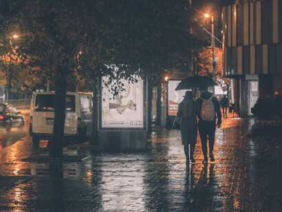 A rain-soaked city street at night, with neon reflections on wet asphalt in a film noir cityscape