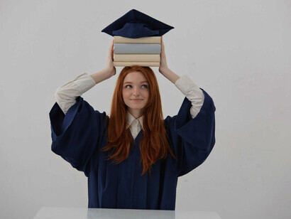 Smiling young female university graduate wearing her academic cap, seated at a table and posing for a photo