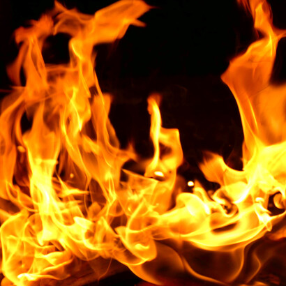 In the stillness of night, flames rise and flicker, casting a warm glow through the surrounding darkness