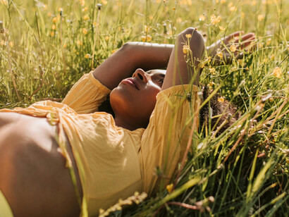Woman in yellow lying on grass, getting sunlight for vitamin D