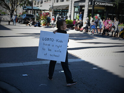 A woman walking by with a sign for LGBTQ+ rights, showing the need for equality and acceptance in society for all individuals, regardless of sexual orientation or gender identity