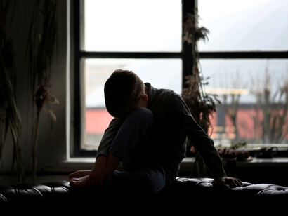 A lone boy sitting in heavy silence, representing the invisible existence of a child who still remembers home