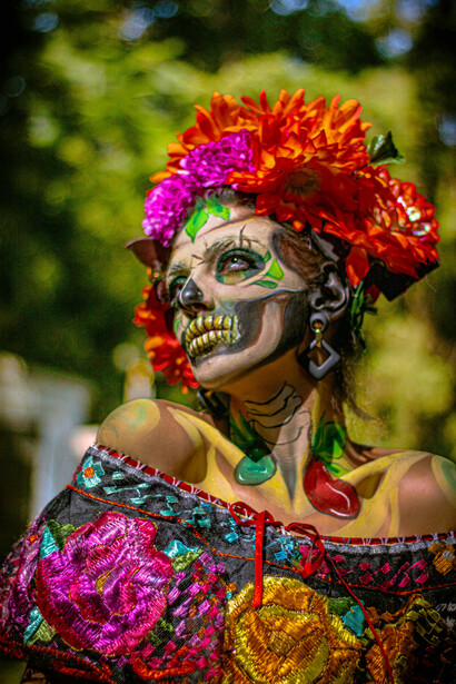 Mexico City, Mexico. A Catrina figure with colorful makeup stands in the cemetery beside a bright Día de los Muertos altar