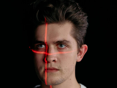 A portrait of a man illuminated by laser lines, representing government surveillance technologies, biometric screening, and facial recognition cameras