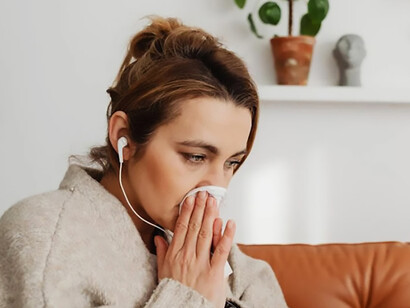 Allergic woman sitting on a couch, wiping her nose with a tissue