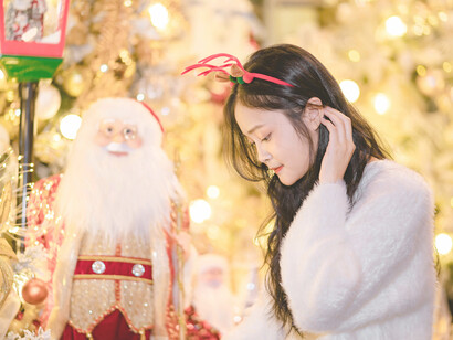 A woman wearing a reindeer headband stands beside a Santa figure while holiday shopping