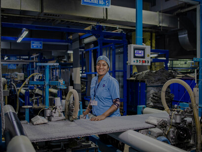 A cheerful factory worker stands at a textile machine, highlighting the human element behind efficient and skilled industrial production