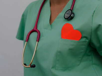 Wearing a green uniform, the healthcare worker has a stethoscope draped around their neck