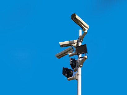 White CCTV cameras on a black post beneath a bright blue sky