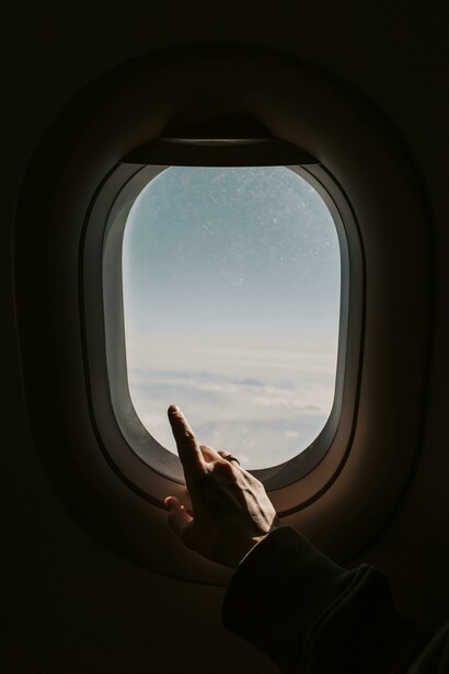 A person points toward the sky while looking out from an airplane window
