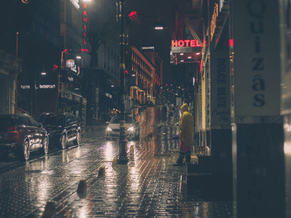 A rain-soaked city street at night, where neon lights bleed across wet asphalt in a film noir atmosphere