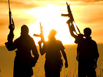 Militants in a desert landscape silhouetted against a sunset