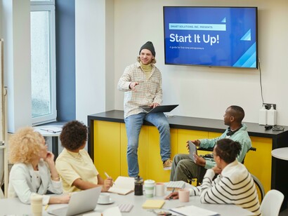 A man leads a startup meeting, explaining ideas as founders collaborate and prepare to pitch their business