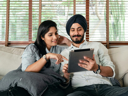 A smiling Punjabi couple sitting on a sofa, enjoying an Indian Punjabi film